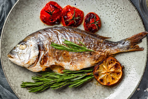 Baked dorado fish on a plate with vegetables top view.